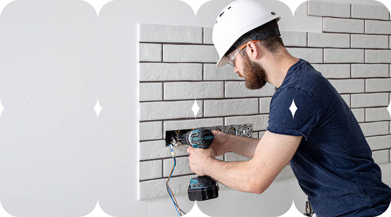 Daxili təmir və tamamlama işləri zamanı fayansla örtülmüş divarda elektrik prizləri quraşdıran tikinti işçisi.