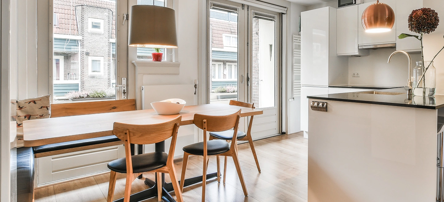 Yemək masası, taxta stullar, böyük pəncərələr və zərif işıqlandırma ilə müasir mətbəx interyeri parlaq və rahat yaşayış məkanı yaradır.